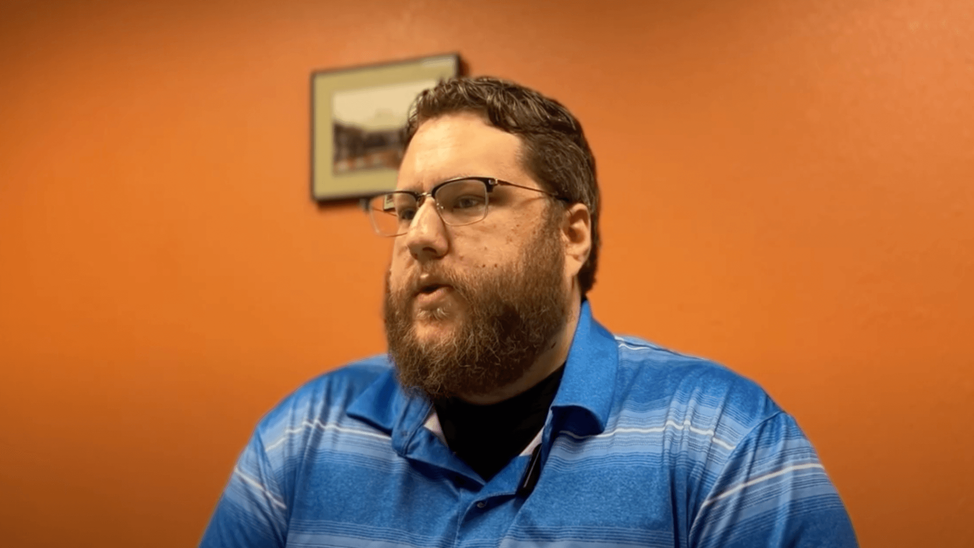 A bearded man in glasses and a blue polo shirt speaking in a Black & White Transportation case study interview