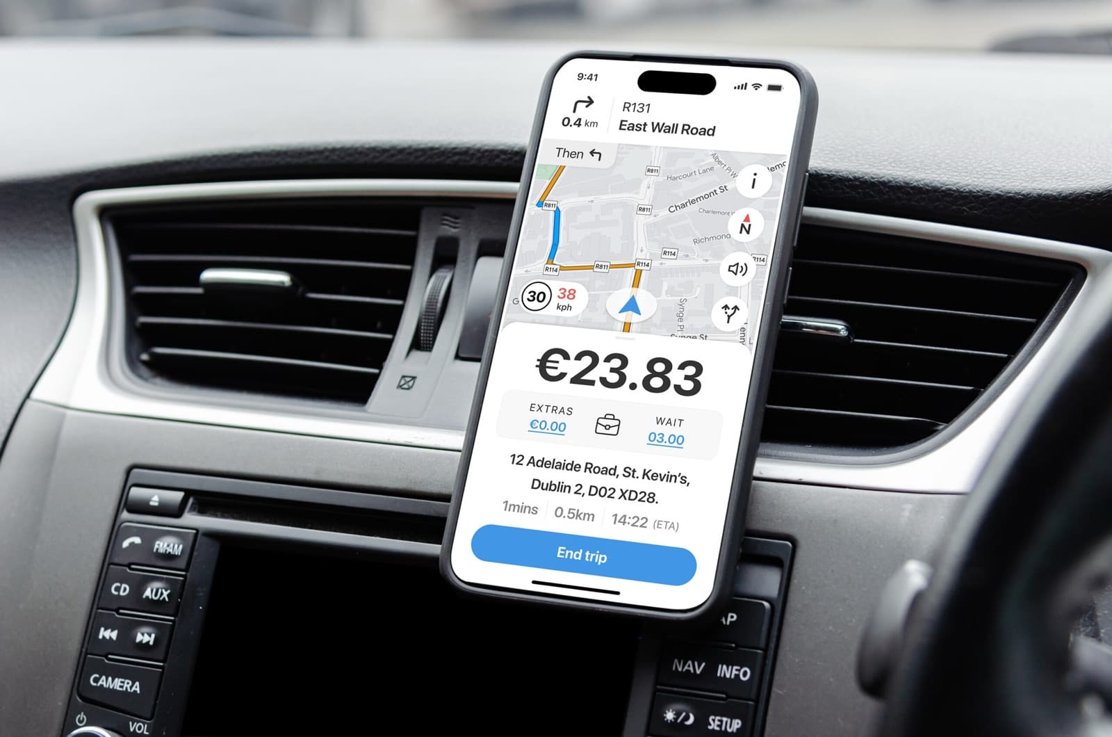 A phone mounted on a car dashboard showing a driver app with turn-by-turn map navigation, the trip fare, destination address and ETA