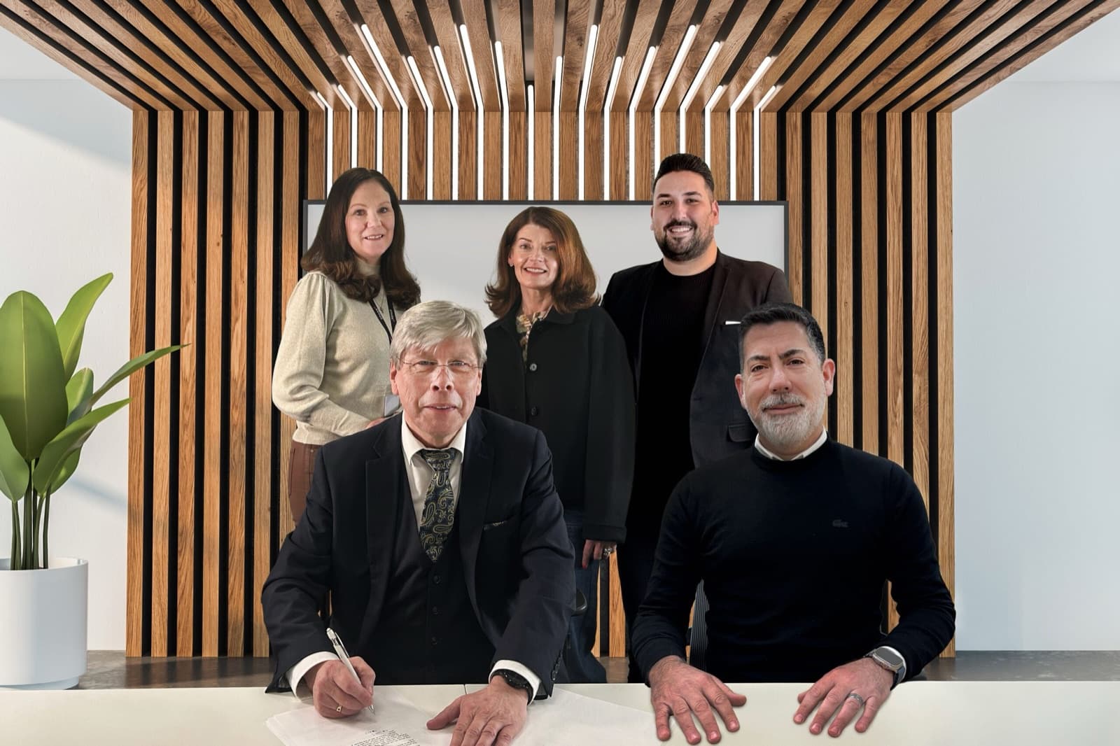 Mick Tope of iCabbi and Ohad Noy of Moovex seated at a desk for the signing of the acquisition, with three colleagues standing behind them