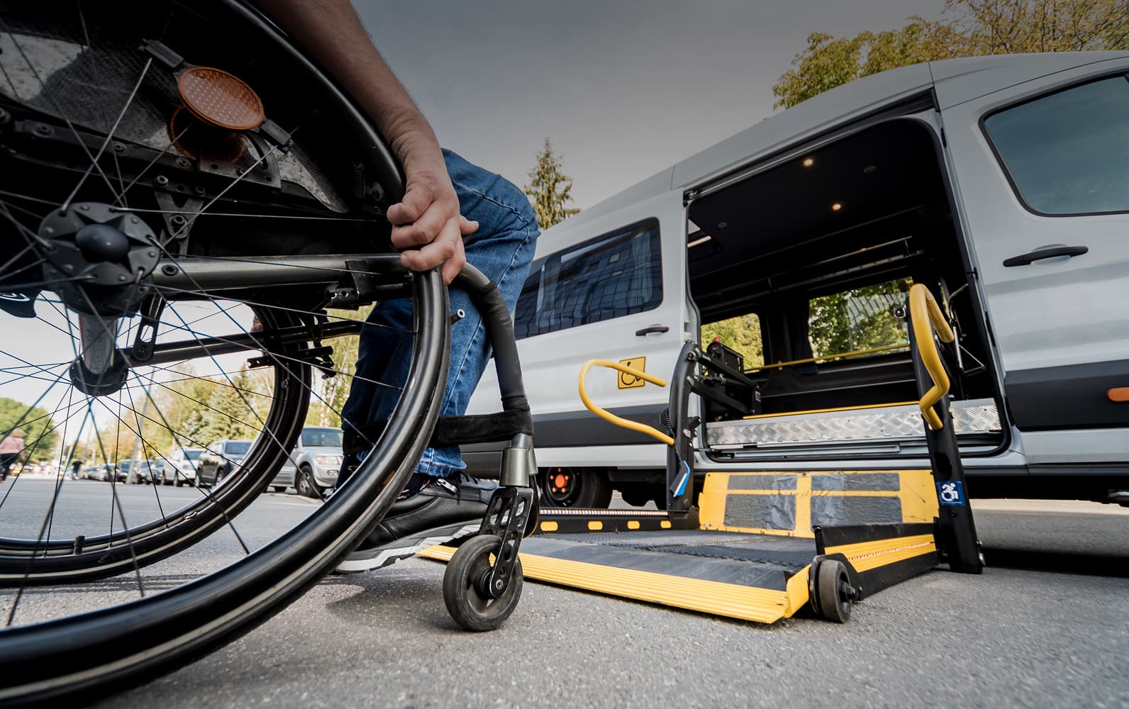 A wheelchair user beside the lowered wheelchair lift of a white accessible van