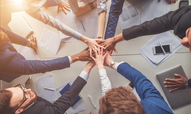 A group of colleagues around a table stacking their hands together in the center