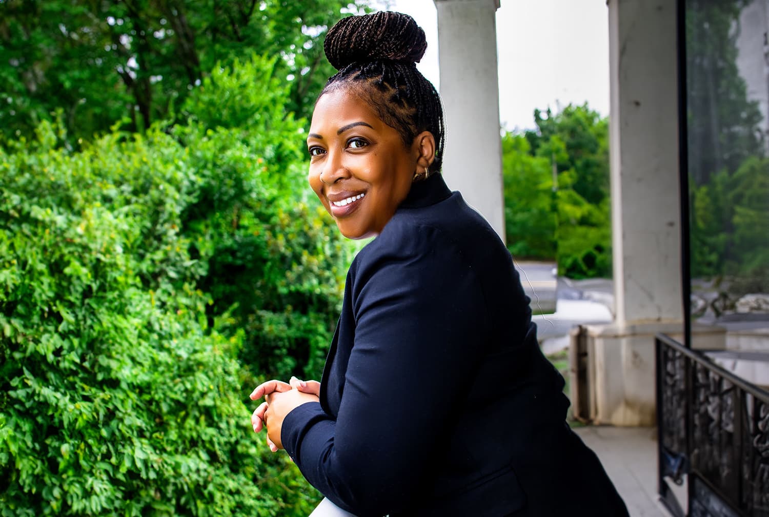 Stephanie Harmon smiling over her shoulder as she leans on a porch railing beside green trees