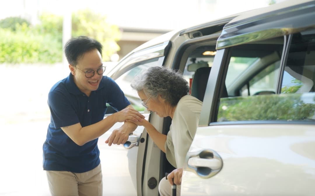 A man helping an elderly woman using a cane step out of a vehicle